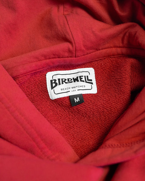 Close-up of the Harmony Hoodie - Red, made in USA, featuring a white Birdwell Beach Britches USA label and a black size M tag visible inside the collar.