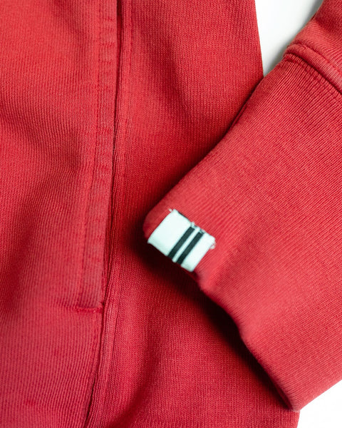 A close-up of the Harmony Hoodie - Red French terry sleeve shows a small white tag with two black stripes near the cuff. The fabric texture and stitching details highlight the quality craftsmanship typical of this premium hoodie, proudly made in the USA.