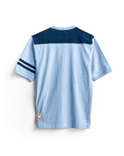 The Special Teez Champ - Arctic Blue/Navy is a light blue, short-sleeve premium t-shirt displayed from the back, featuring a navy yoke across the shoulders and two navy stripes on the left sleeve. Made from USA-grown cotton in a relaxed fit, it includes a small label near the left hem.