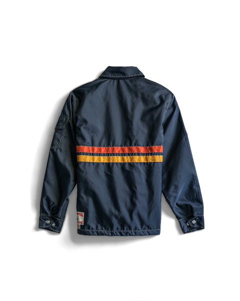The Comp Jacket 26 - Navy/Gold/Paprika is shown from the back, featuring horizontal gold and paprika stripes across the midsection, buttoned cuffs, and a small label near the bottom hem. Crafted in the USA with legendary SurfNyl durability, this jacket combines timeless style with lasting quality.