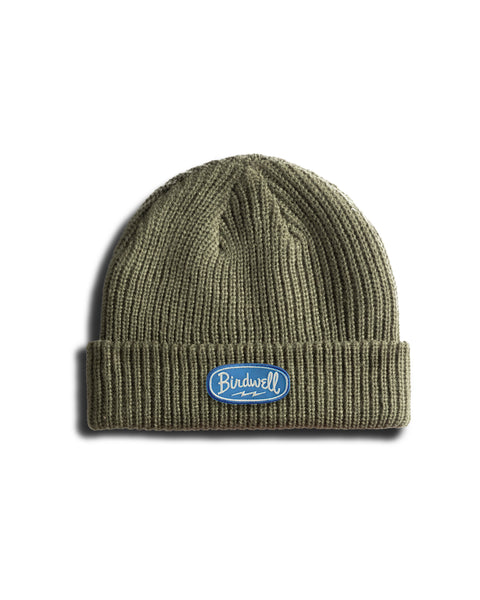 The Powerbird Watchcap - Army is an olive green ribbed beanie with a folded brim. It features a blue and white Powerbird patch on the front, showcasing the classic fisherman style against a white background.