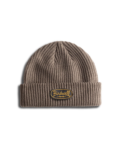 A walnut-colored, wide ribbed fisherman style beanie with a folded cuff featuring a yellow and black Powerbird patch logo on the front, shown against a white background.