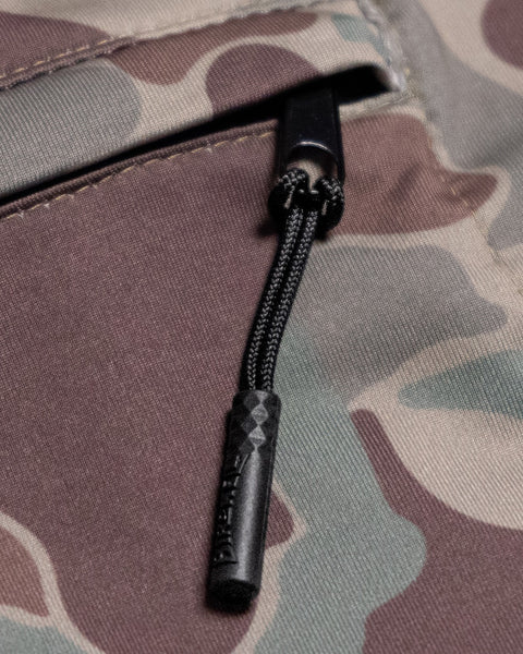 Close-up of the black zipper pull on the green and brown camouflage fabric of the Sunteez Hoodie - Frogskin Camo, highlighting the textured zipper and distinctive camo pattern. This moisture-wicking material, featured in UPF50+ sun shirts made in the USA, ensures comfort and sun protection for your outdoor adventures.