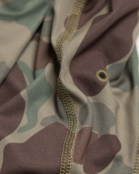 Close-up of the Frogskin Camo fabric on the Sunteez Hoodie, showing distinct green, brown, and beige camouflage shapes with visible stitching and a small circular mark near the seam. This UPF50+ shirt offers advanced sun protection.