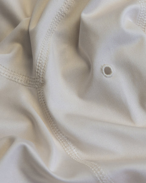 Close-up of the light-colored fabric of the Sunteez Hoodie - Bone, highlighting the visible stitching, soft folds, and a small round hole near the center. The texture and seams stand out, showcasing the quality craftsmanship of this UPF50+ sun shirt made in the USA.