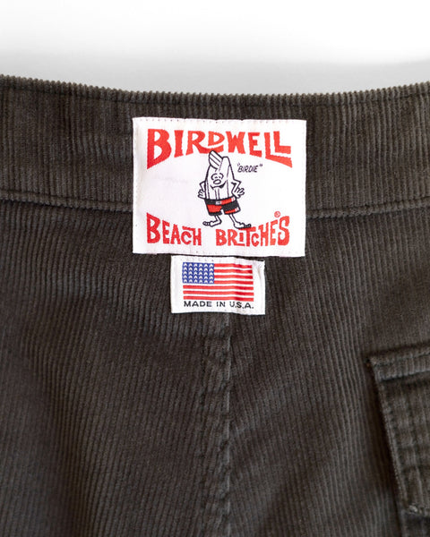 Close-up of the corduroy waistband on the Classic Corduroy Shorts - Brown, featuring two labels: one with Birdwell Beach Britches and a cartoon bird, and another displaying the American flag and MADE IN U.S.A. The adjustable drawcord waist ensures a perfect fit.