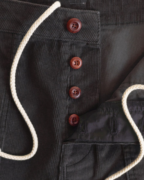 Close-up of the Classic Corduroy Shorts - Brown, showcasing dark corduroy fabric with four brown buttons, an adjustable waistband with a white drawstring, and the partially open waistband revealing black inner lining.