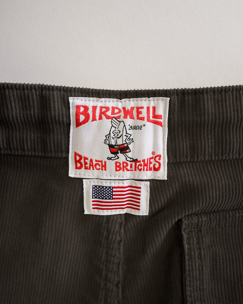 Classic Corduroy Pants - Brown in 100% cotton corduroy featuring a white brand label with a cartoon character, the text Birdwell Beach Britches, and a small American flag patch.
