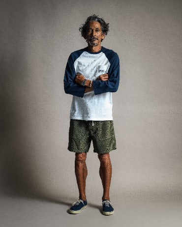 A man with arms crossed wearing a navy and white baseball-style shirt and olive green Classic Corduroy Shorts - Sand with a drawcord waist.