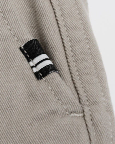 Close-up of a tan cotton twill pocket on Stockman Chino Shorts - Bone, featuring a small black and white striped tag sewn into the seam.