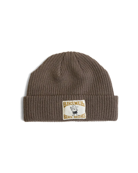 Walnut License Plate Watchcap featuring a brown ribbed fisherman beanie with a folded cuff and a rectangular license plate patch with a cartoon character and the text Birdwell Beach Britches.