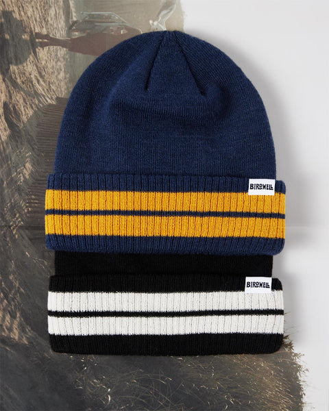 Front of the Comp Stripe Beanie in Navy and Black, sitting on top of an old beach photograph