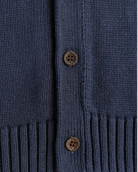 Close-up of a blue knitted cardigan with brown buttons on a matching fabric background
