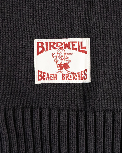 Close-up of a black knit sweater with a 'Birdwell Beach Britches' license plate label.