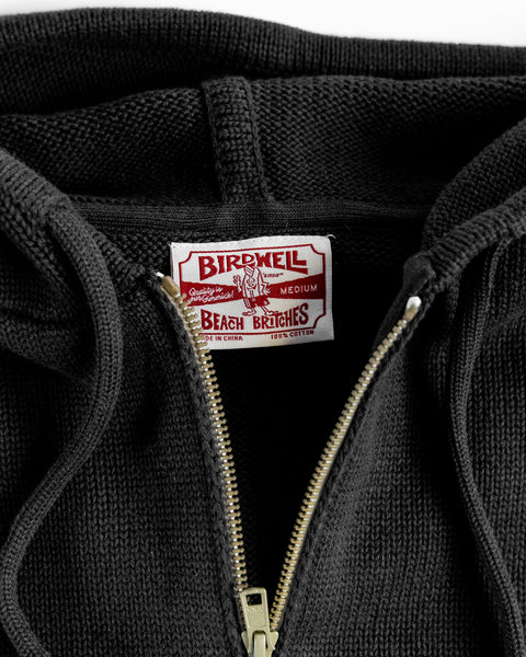 Close-up of a black hoodie with a Birdwell label and zipper on a white background.