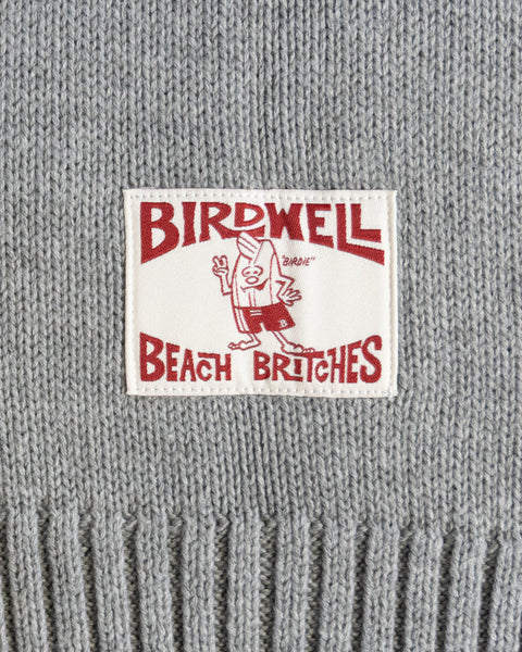 Close-up of a gray knit sweater with a 'Birdwell Beach Britches' license plate label.