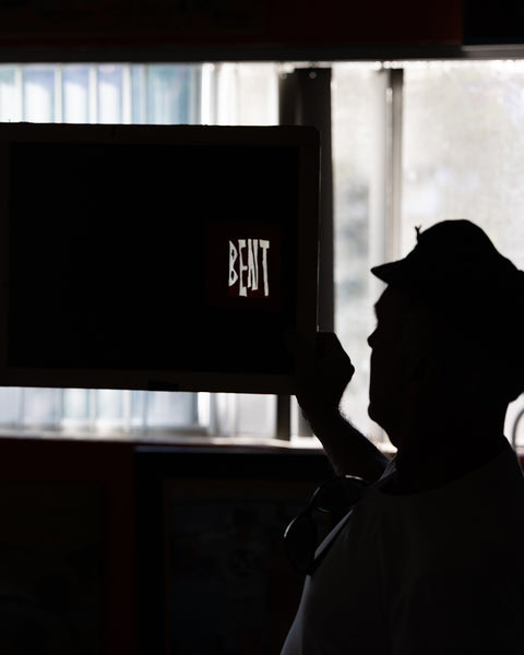 Brian Bent holding up the screen with BENT displayed, silhouette against a blurred indoor background