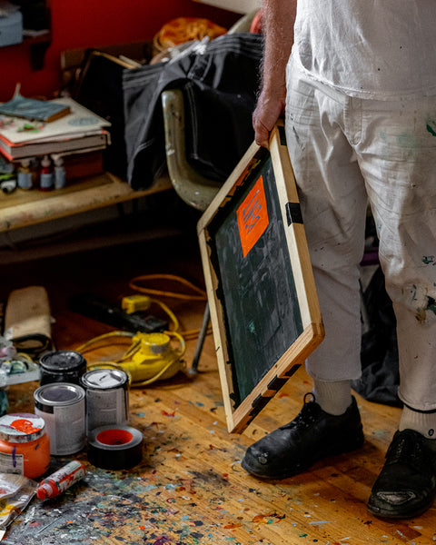 Brian holding the screen in his art studio with paint cans and tools on the floor.