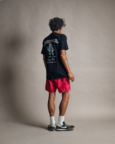 A person seen from behind wearing a black 61 T-Shirt - Black, bright pink shorts, white socks, and athletic shoes.