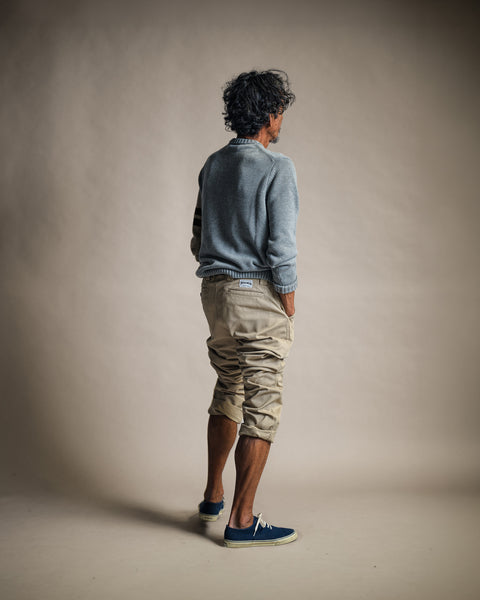 A man standing with his back to the camera, wearing a grey sweater and Stockman Chino Pants - Khaki with his hands in his pockets.