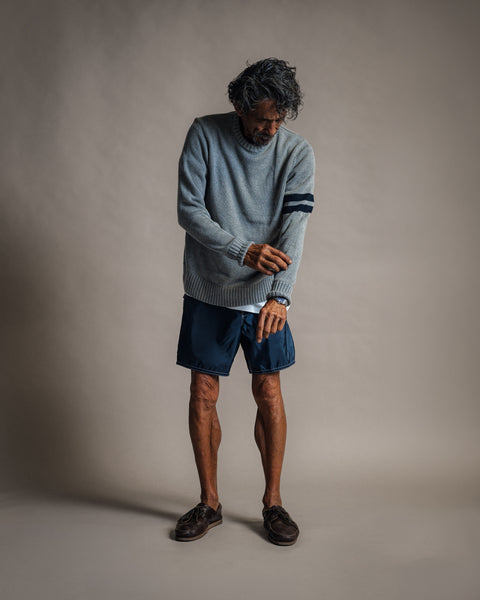 A man wears a gray and navy Comp Stripe Sweater with navy shorts and brown boat shoes.