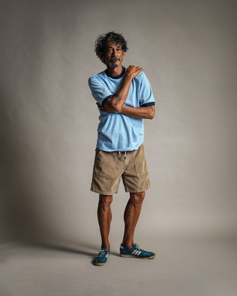 A man wears a light blue t-shirt and Classic Corduroy Shorts - Sand with an adjustable drawcord waist while standing against a neutral background.