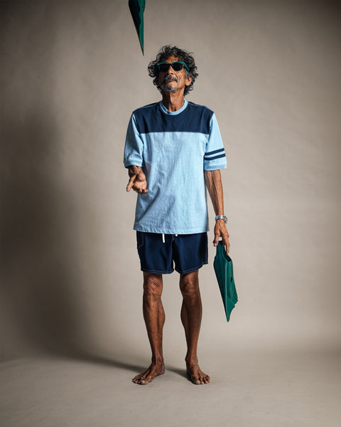 A man wearing a Special Teez Champ - Arctic Blue/Navy t-shirt, navy shorts, and sunglasses, juggling a swim fin.