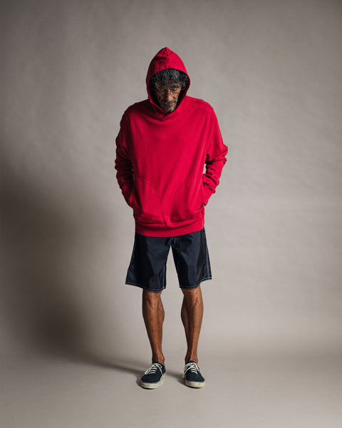 A man wearing a red Harmony Hoodie - Red premium French terry hooded sweatshirt with the hood up, dark shorts, and sneakers.