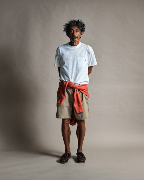 A man wearing a High Tee Pocket - Vintage White t-shirt, khaki shorts, and a bright orange sweatshirt tied around his waist.