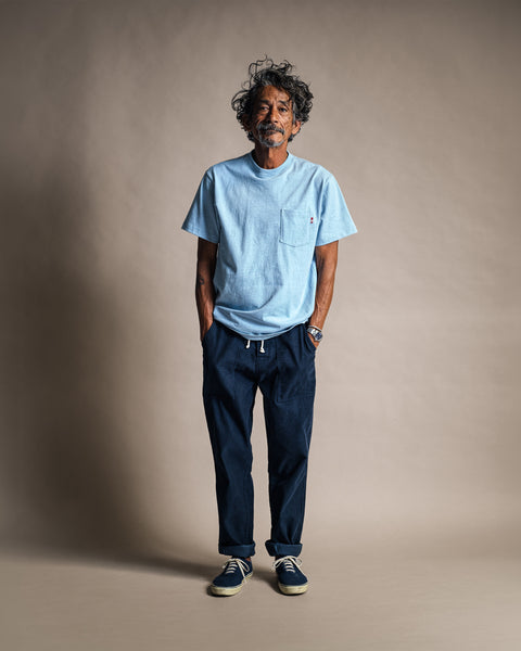 A man wearing a High Tee Pocket - Arctic Blue 100% cotton light blue crew neck t-shirt with a chest pocket and dark navy trousers.