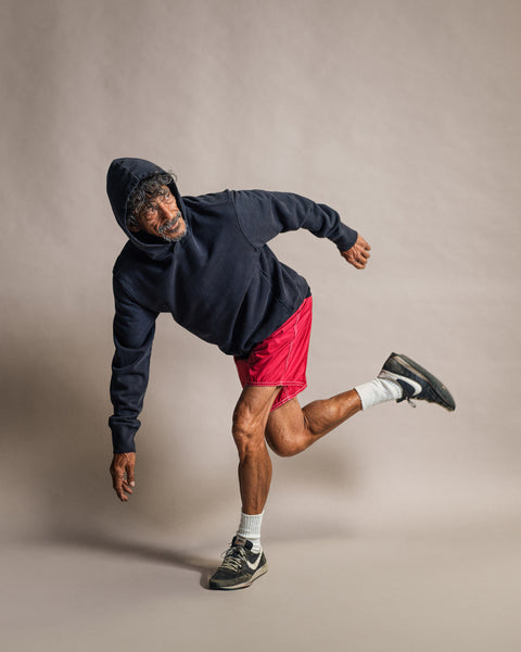 A man in a Faded Black Harmony Hoodie and red shorts striking a dynamic, athletic pose.