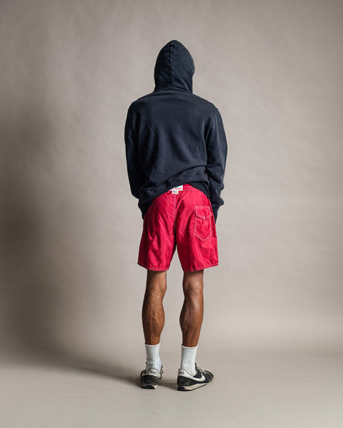 A person seen from behind, wearing a faded black Harmony Hoodie, bright red shorts, white crew socks, and sneakers.