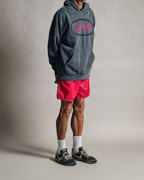 A person wearing a relaxed fit, faded black Mashed Potato Hoodie with a pink circular screen-print graphic, bright pink shorts, white crew socks, and sneakers.