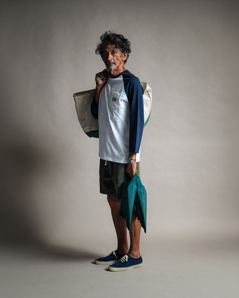 A man wearing a Special Teez Pastime - Vintage White/Navy 3/4 sleeve raglan t-shirt and green shorts, holding a large canvas bag on his shoulder and swim fins in his hand.