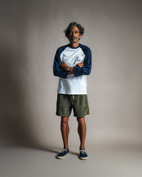 A man with arms crossed wears a Special Teez Pastime - Vintage White/Navy relaxed fit 3/4 sleeve raglan t-shirt with a chest pocket, olive green shorts, and navy blue sneakers.