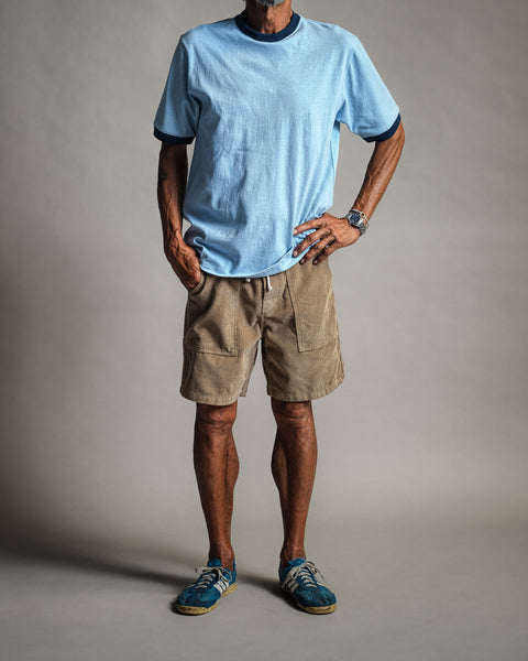 A man wears a light blue t-shirt and Classic Corduroy Shorts - Sand, featuring front patch pockets and an adjustable drawcord waist.