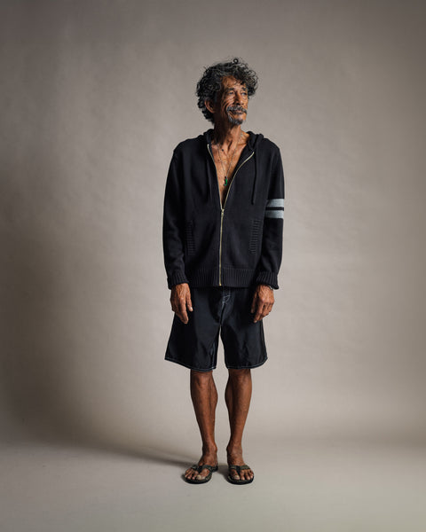 A man wearing a black Comp Zip Sweater - Black/Gray with a grey stripe on the sleeve, black shorts, and sandals.