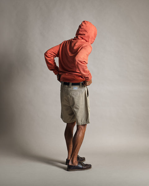 A person seen from behind, wearing an orange hooded sweatshirt and Stockman Chino Shorts - Moss with a black belt and brown boat shoes.