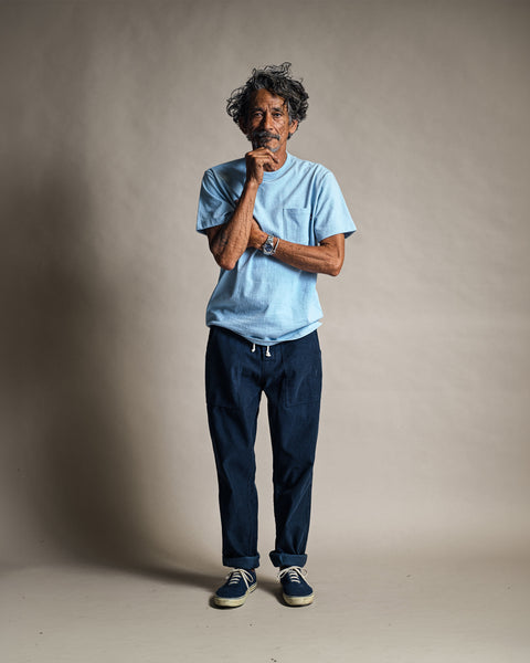 A man wearing a light blue t-shirt and Classic Corduroy Pants - Navy with a drawstring waist stands with his hand to his chin.
