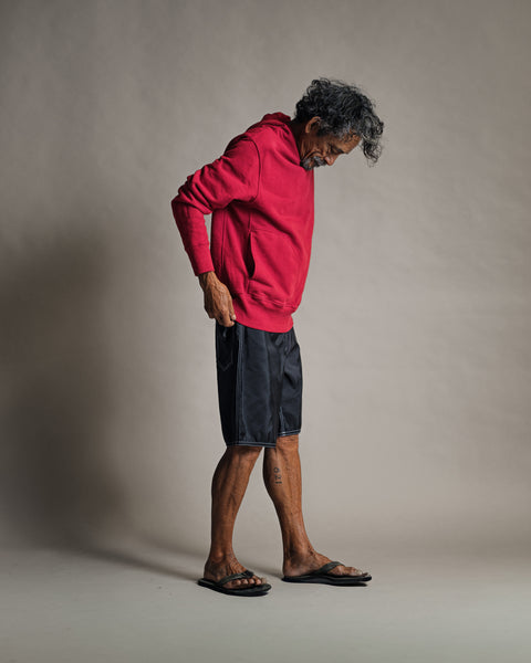 A man stands in profile wearing a red Harmony Hoodie - Red and black shorts.